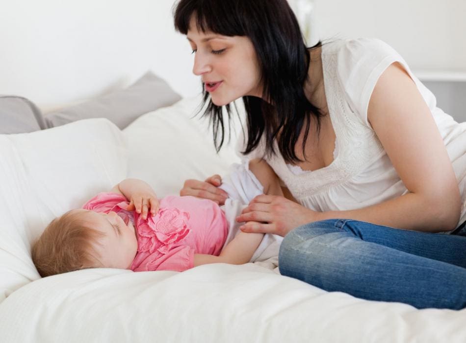 Woman interacting with baby on bed.