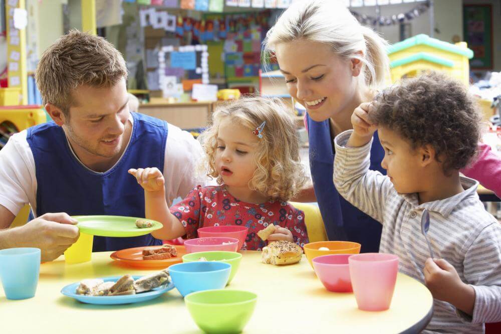Children and teachers eating at daycare table.