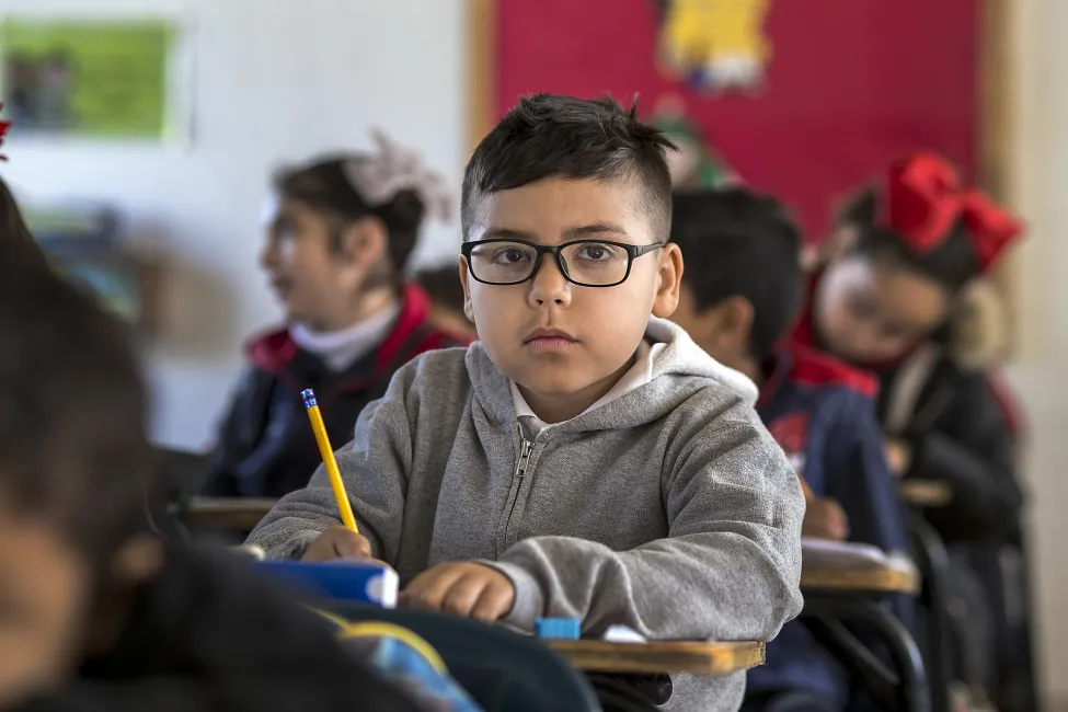 Student in classroom holding a pencil attentively.